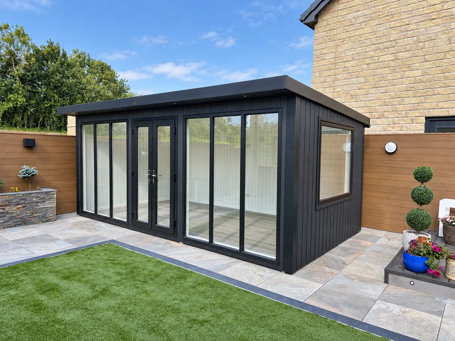 Black composite Chippenham garden room with full-height glazing beside a paved garden